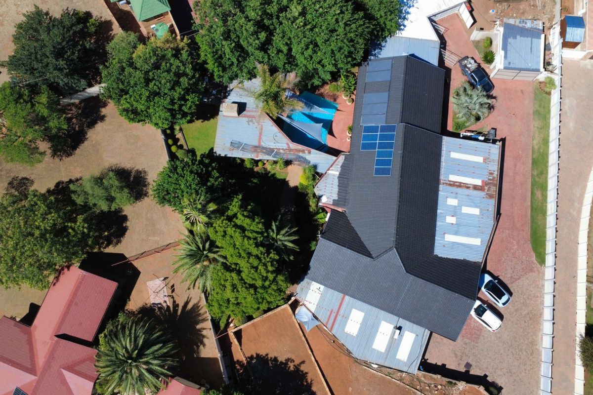 Aerial view of the property showcasing the roof structure with solar panels, paved driveway, and swimming pool area.