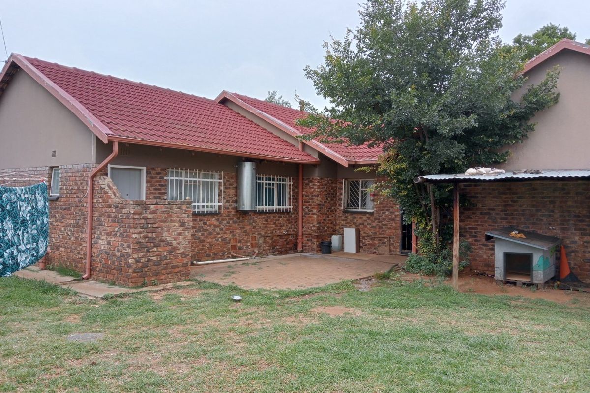 Rear view of a brick-faced house featuring a tiled roof, paved patio area, and security bars on windows, set within a garden space.