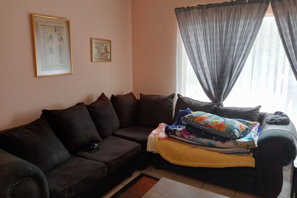 A living room area featuring tiled flooring and natural light from a window with curtains.