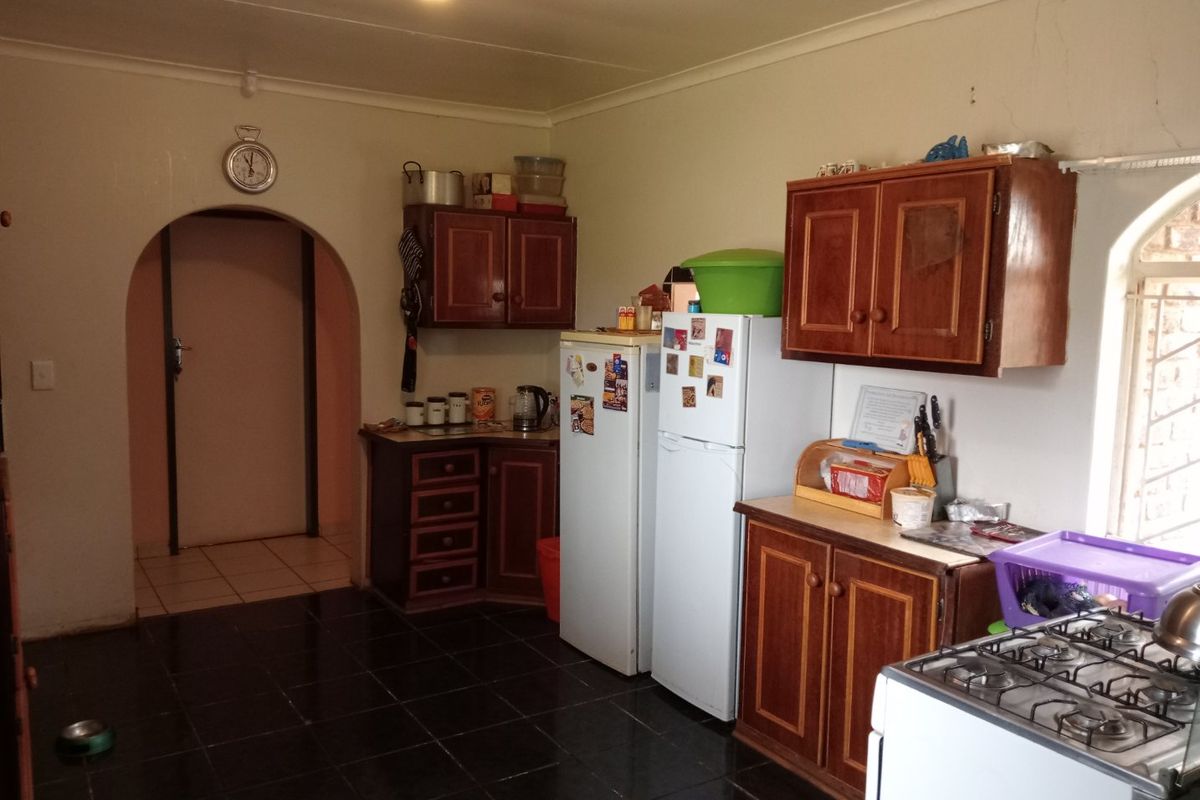 A functional kitchen featuring dark tiled flooring, wooden cabinetry, and an arched doorway leading to an adjacent room.