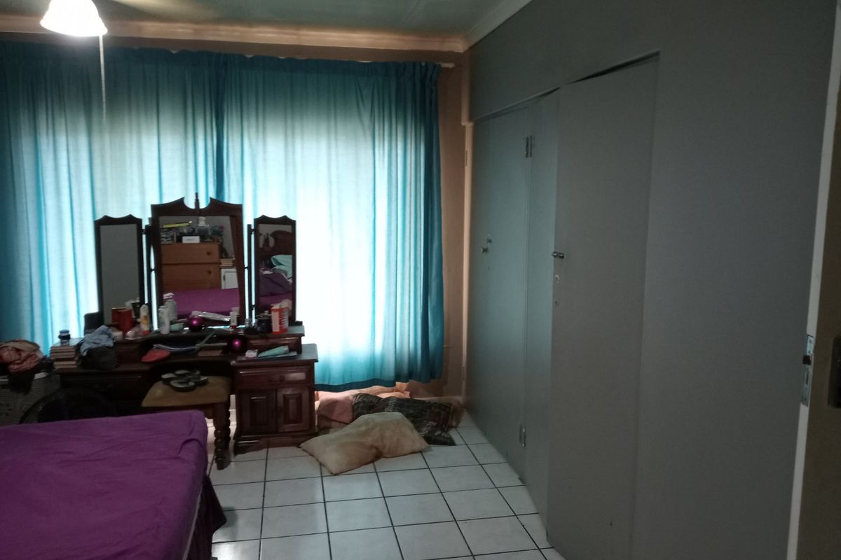 A bedroom featuring tiled flooring, built-in cupboards, and a ceiling fan, offering a functional space with potential for modernization.