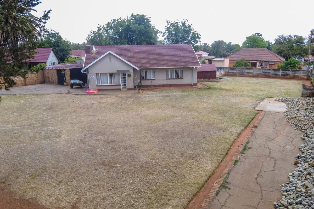Rear view of a detached house featuring a large garden, tiled roof, brick facade, and a concrete driveway with a carport.