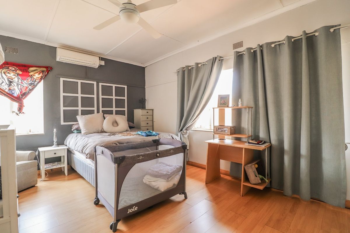 A bedroom featuring laminate flooring, a ceiling fan, and a wall-mounted split-system air conditioner.