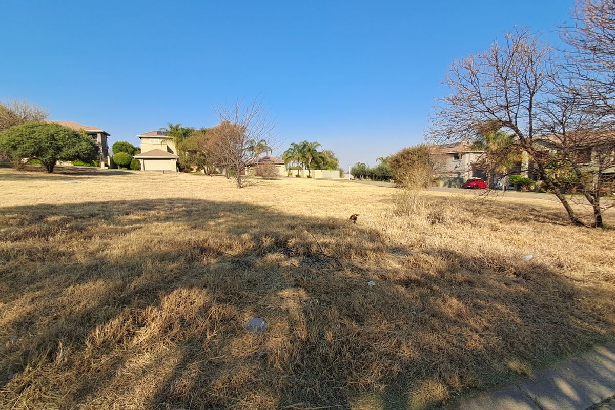 A wide-angle view of a vacant residential plot featuring dry grass, situated in a developed suburban neighborhood.