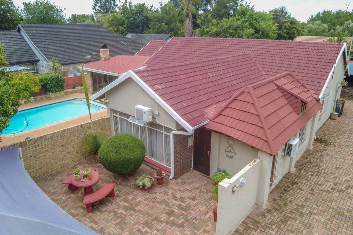 Aerial view of the property featuring a tiled roof, paved patio area, swimming pool, and brick boundary walls.