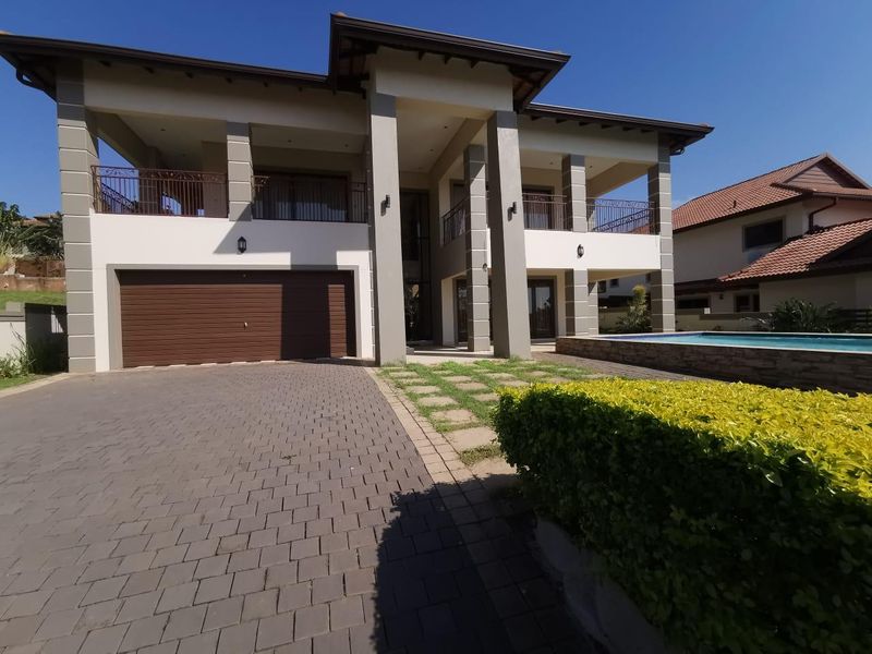 Modern double-story residence featuring a paved driveway, integrated double garage, upper-level balcony, and a private swimming pool.
