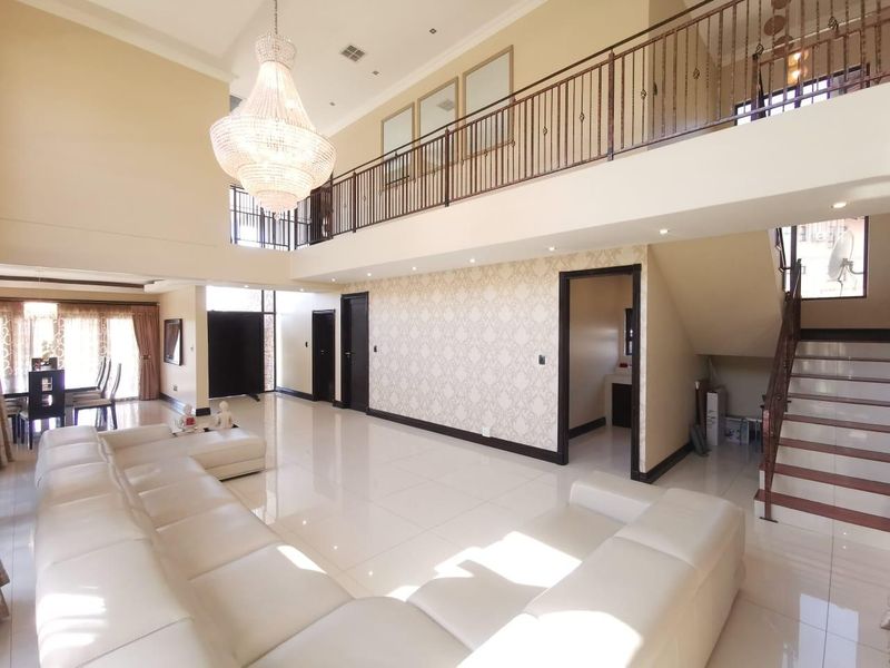 Spacious double-volume living area featuring a grand crystal chandelier, polished porcelain tiles, and an elegant mezzanine landing with a wrought iron balustrade.