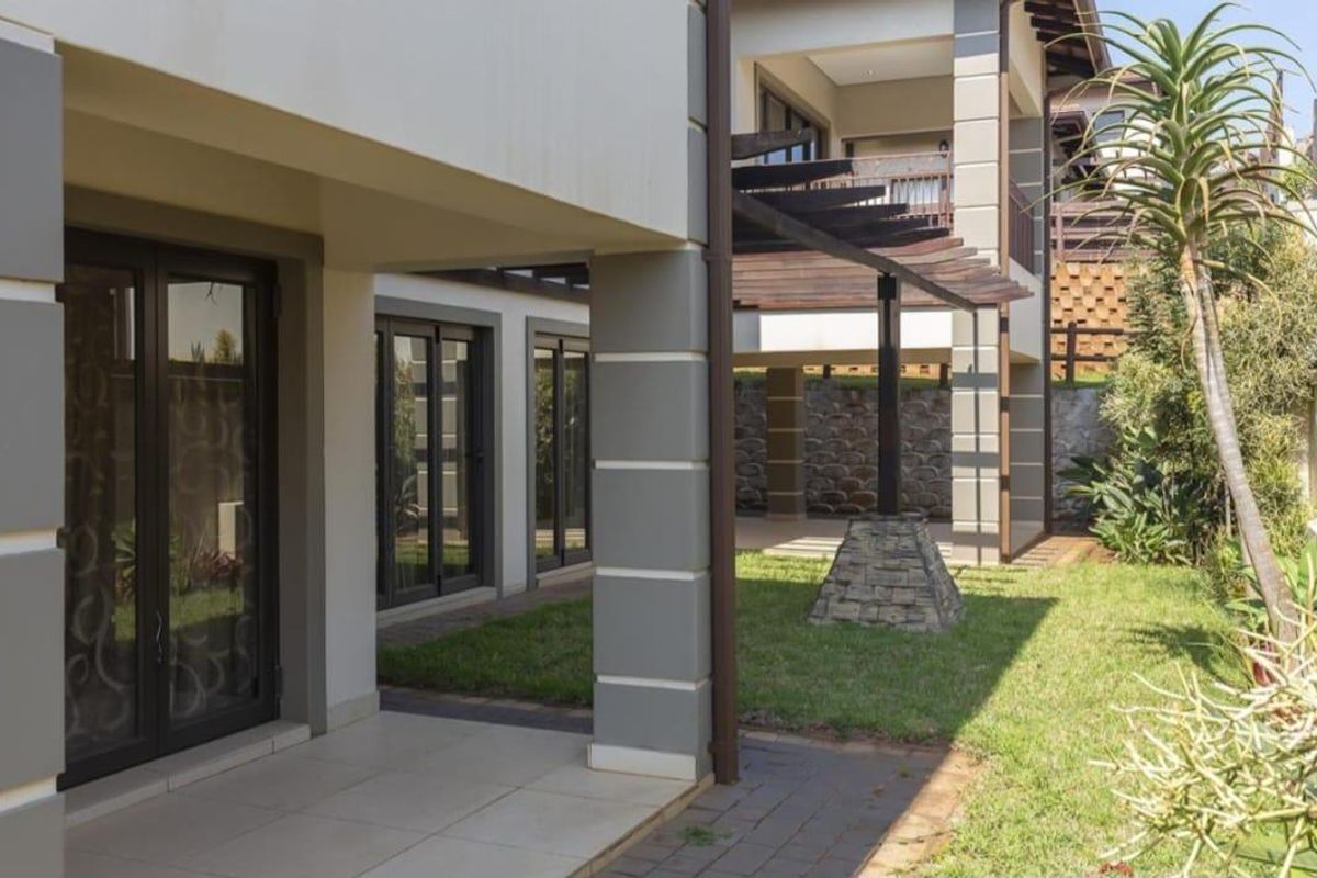A well-maintained rear exterior featuring a covered patio, timber pergola, stone accents, and a landscaped garden with paved walkways.