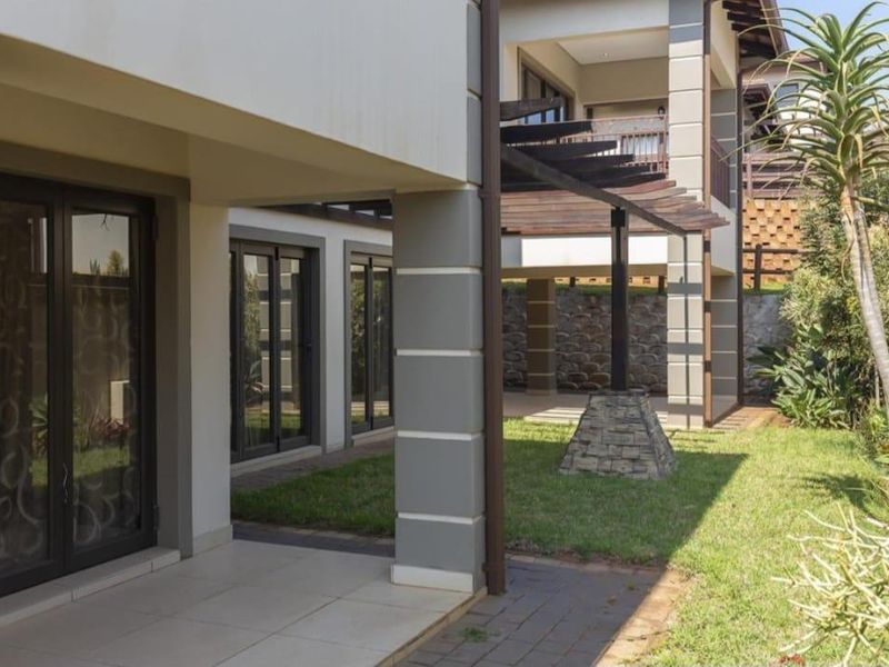 A well-maintained rear exterior featuring a covered patio, timber pergola, stone accents, and a landscaped garden with paved walkways.