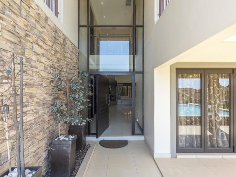 A grand double-volume entrance featuring a striking stone-clad feature wall, large glass panels, and modern tiled flooring leading into the home.