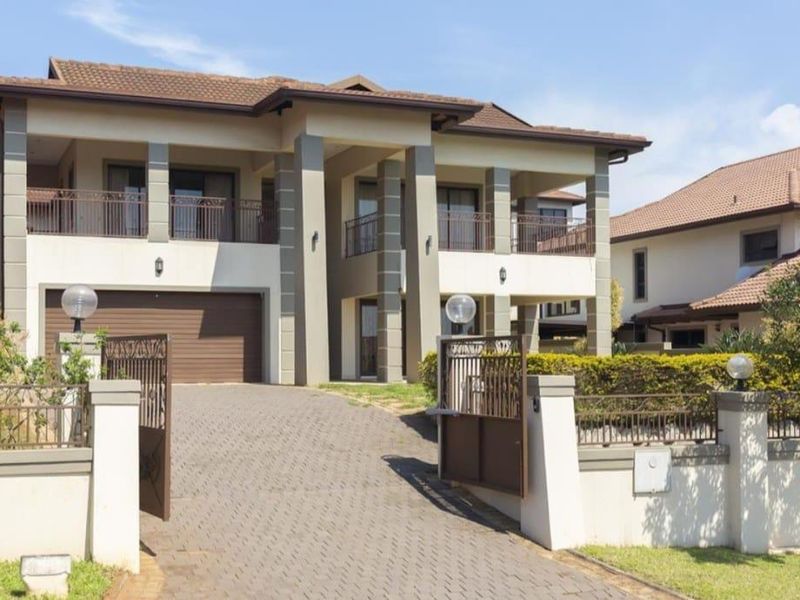 A modern double-story residential property featuring a paved driveway, double garage, and upper-level balconies, secured by a perimeter wall and gate.