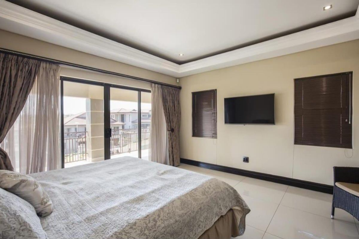Spacious bedroom featuring a tray ceiling, recessed lighting, tiled floors, and large sliding glass doors opening onto a private balcony.