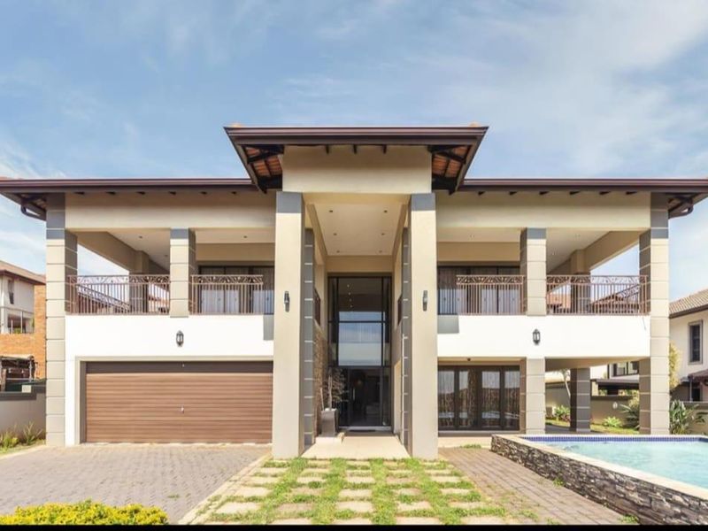 Modern double-story residence featuring a double garage, expansive upper-level balcony, and a private swimming pool with stone-clad water feature.