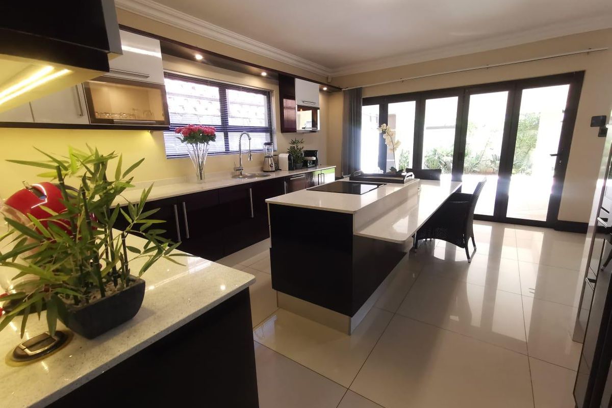 Modern kitchen featuring dark gloss cabinetry, white quartz countertops, a central island with a built-in hob, and large bi-fold doors leading to the outdoors.