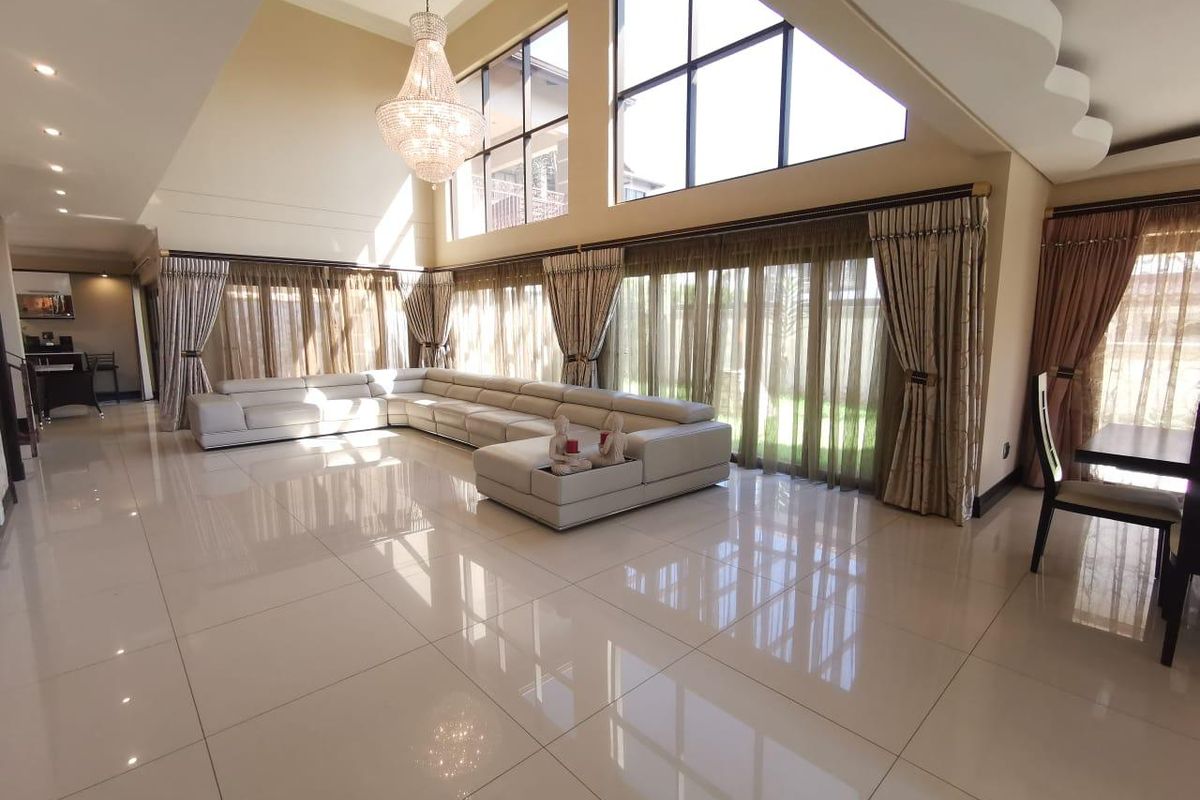 Spacious living room featuring double volume ceilings, large windows for natural light, polished porcelain tile flooring, and an elegant crystal chandelier.