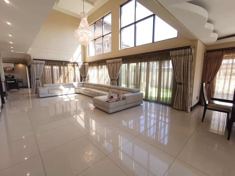 Spacious living room featuring double volume ceilings, large windows for natural light, polished porcelain tile flooring, and an elegant crystal chandelier.