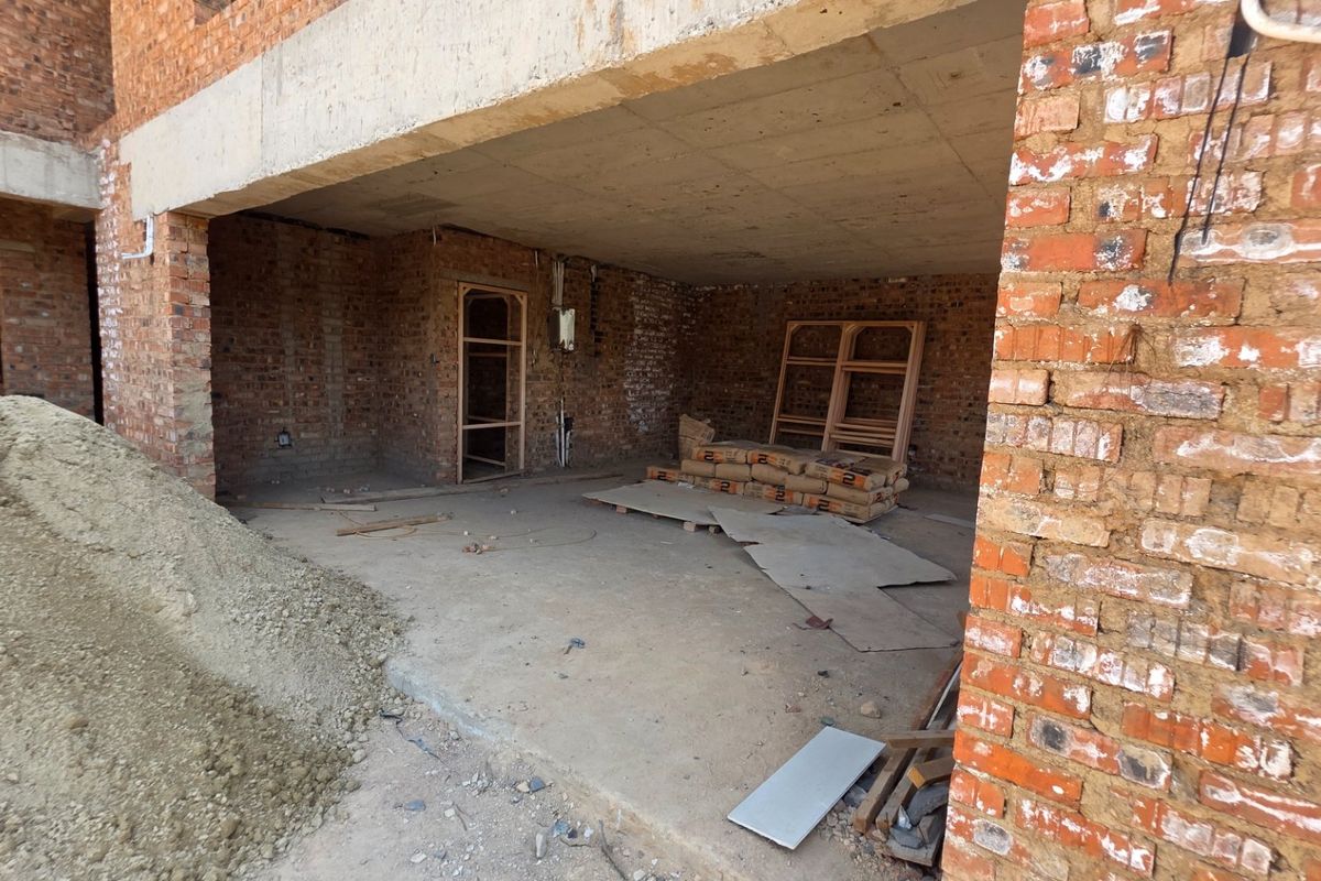 An unfinished exterior patio area under construction, featuring exposed brick walls and a raw concrete ceiling, awaiting final finishes and flooring.