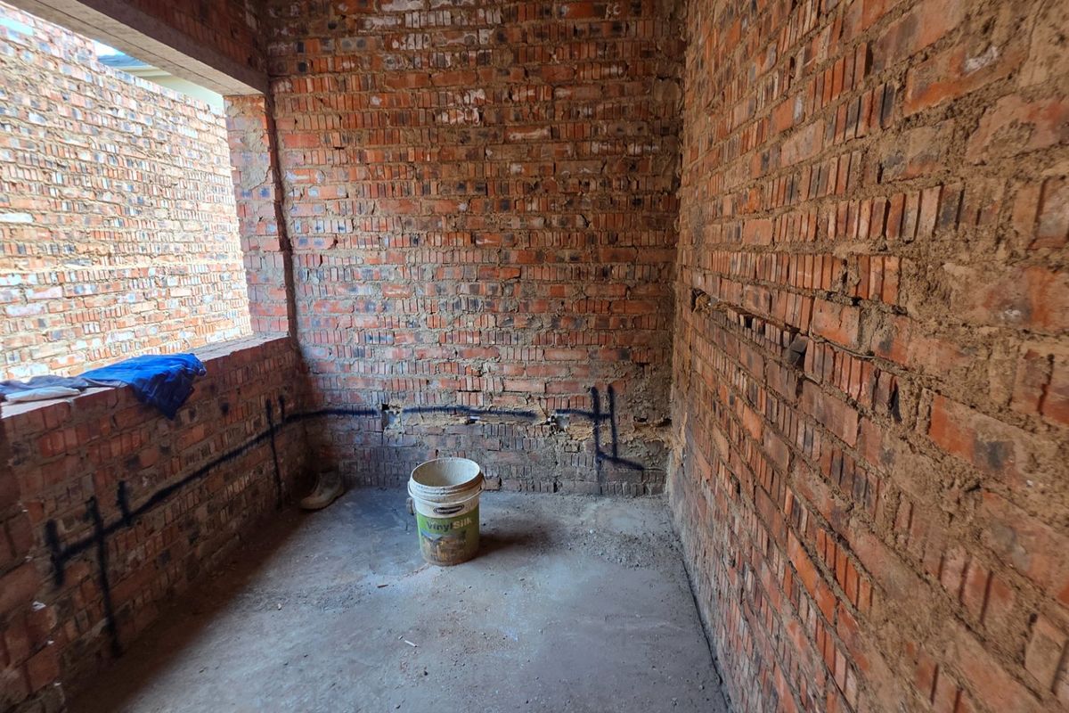 An unfinished bedroom space featuring exposed brick walls and concrete flooring, currently in the early stages of construction.