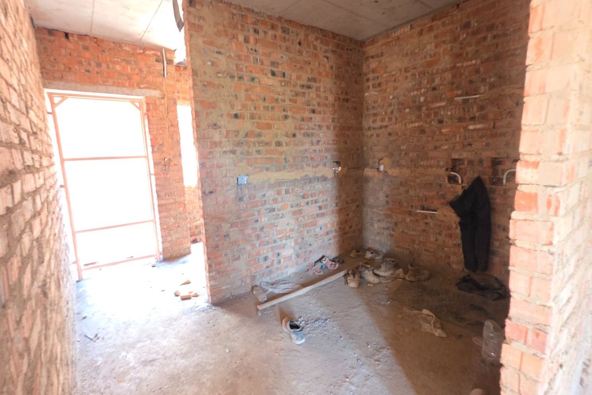 An unfinished kitchen area in shell condition featuring exposed brick walls and visible plumbing rough-ins, ready for complete fit-out and renovation.