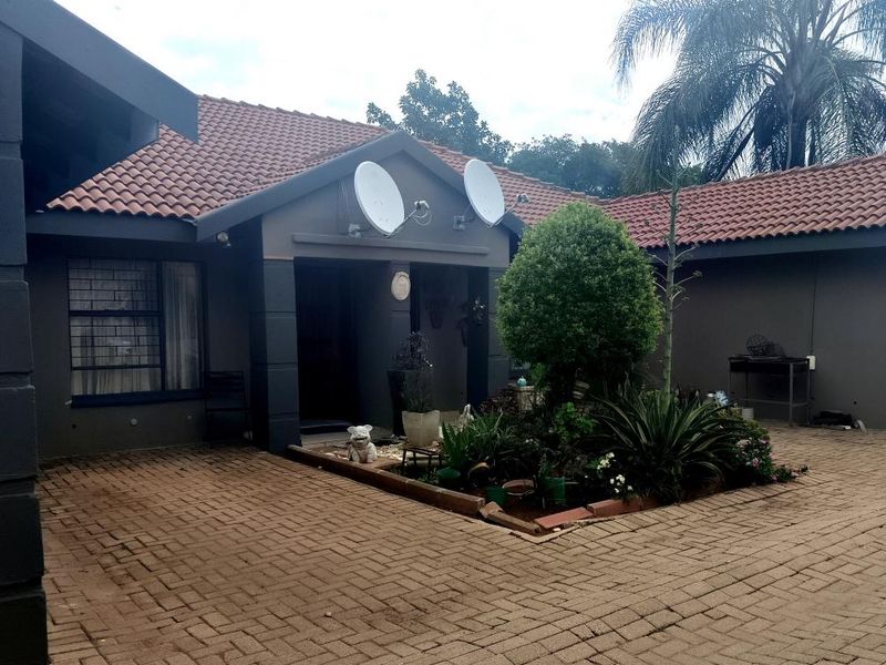 Front exterior view of a townhouse featuring a paved driveway, tiled roof, and a central landscaped garden bed with built-in planter.