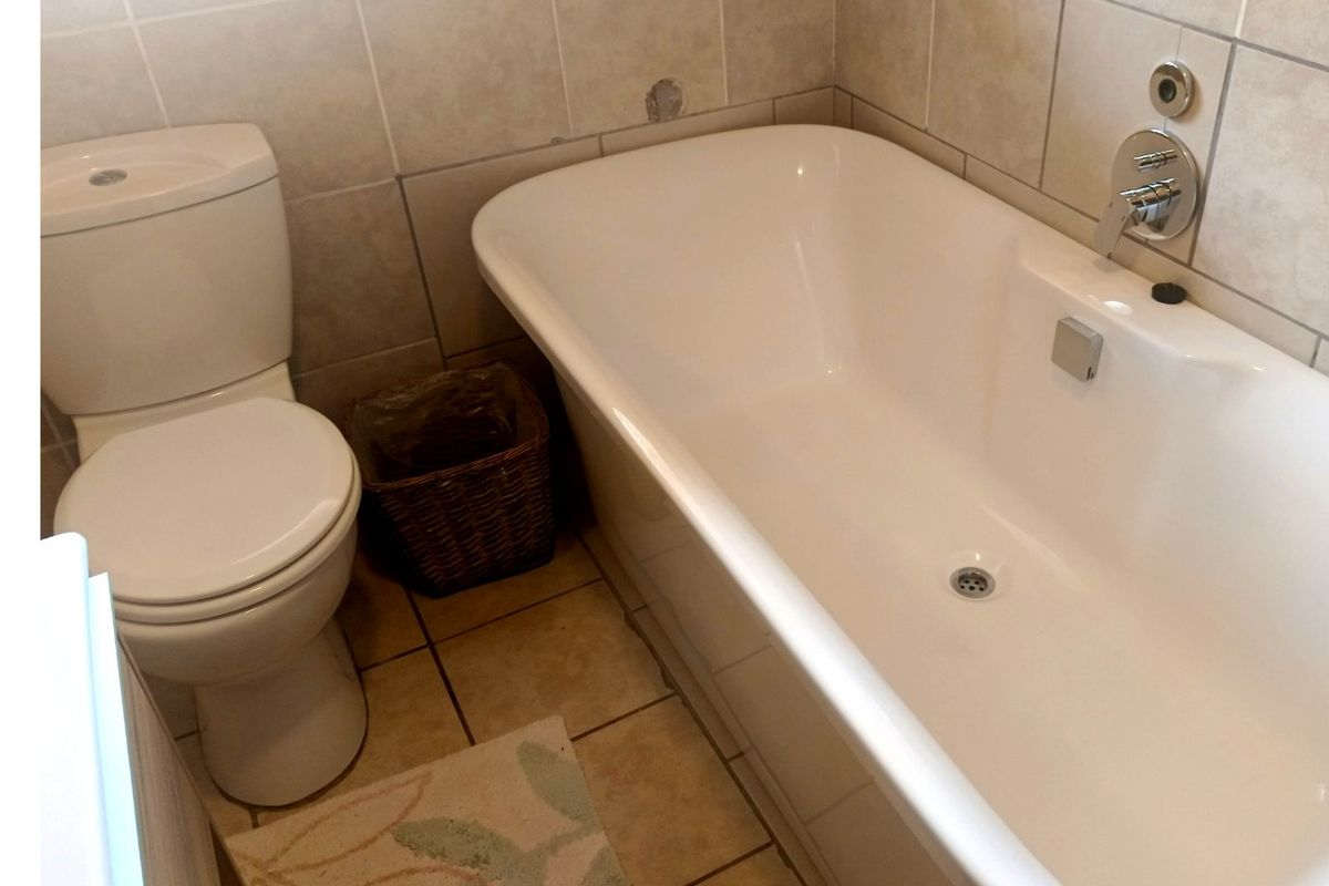 A functional bathroom featuring a standard bathtub and toilet with neutral ceramic tiling throughout.