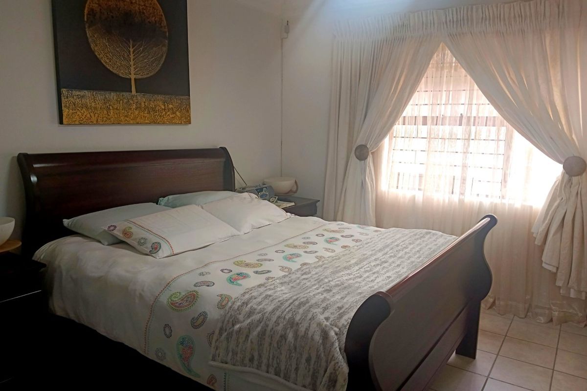 A functional bedroom featuring tiled flooring and a window fitted with security bars, providing natural light.