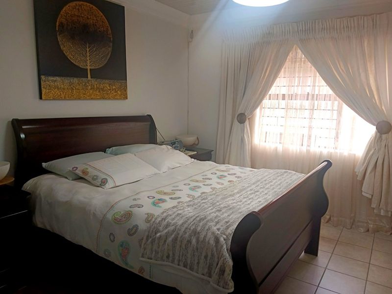 A functional bedroom featuring tiled flooring and a window fitted with security bars, providing natural light.