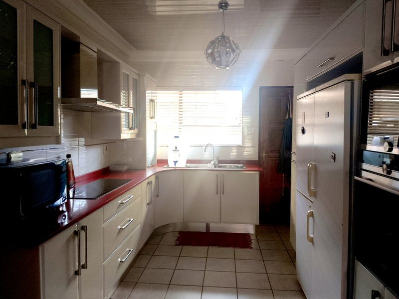 A functional kitchen featuring white cabinetry, red countertops, tiled flooring, and integrated appliances, illuminated by natural light from the window.