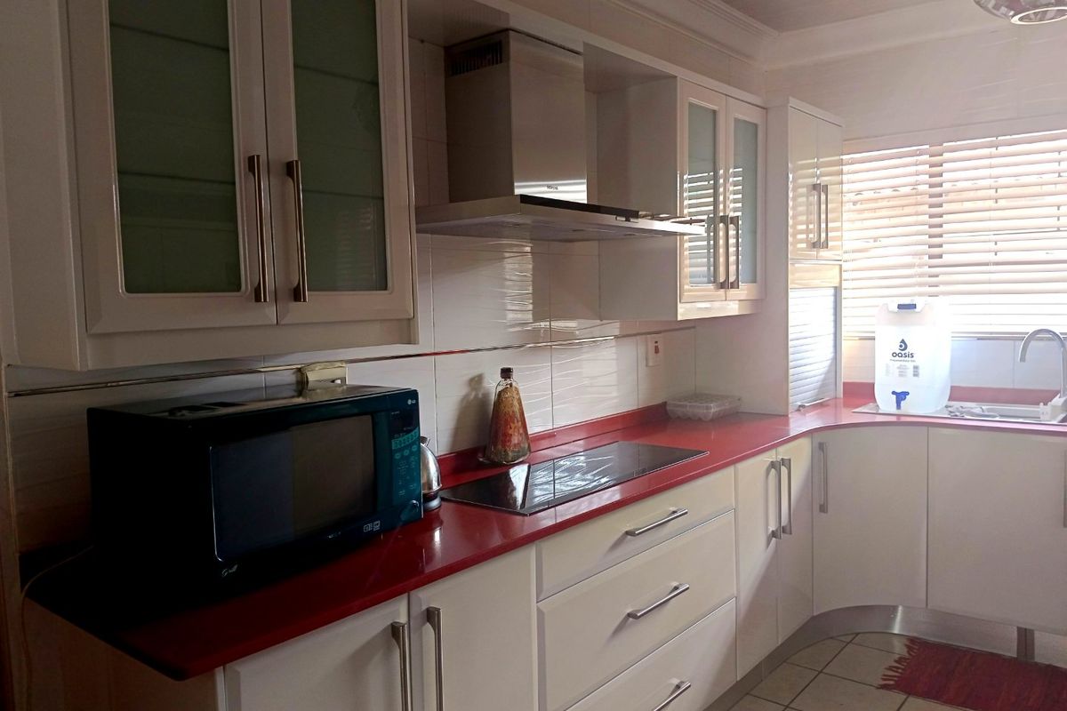 A functional kitchen featuring white cabinetry, a bold red countertop, integrated hob, stainless steel extractor fan, and tiled flooring.