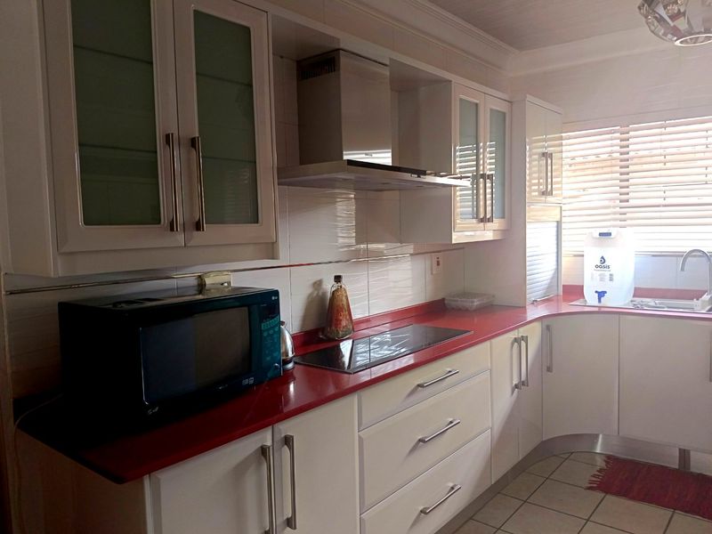 A functional kitchen featuring white cabinetry, a bold red countertop, integrated hob, stainless steel extractor fan, and tiled flooring.