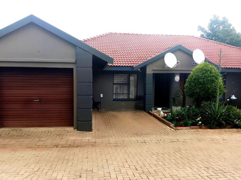 Front elevation of a townhouse featuring a paved driveway, single garage, and tiled roof with satellite dish installations.