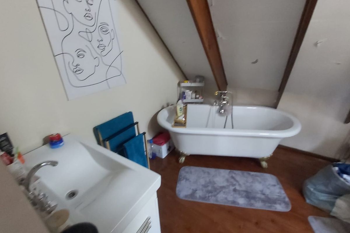 Attic-style bathroom featuring a classic clawfoot bathtub, pedestal basin, and exposed timber rafters under a sloped ceiling.