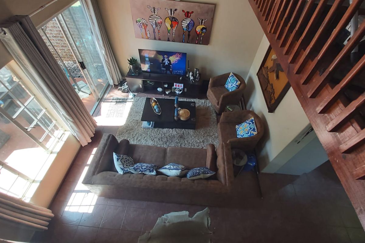 A high-angle view of a living room featuring tiled flooring, a wooden staircase balustrade, and sliding glass doors leading to an outdoor patio area.