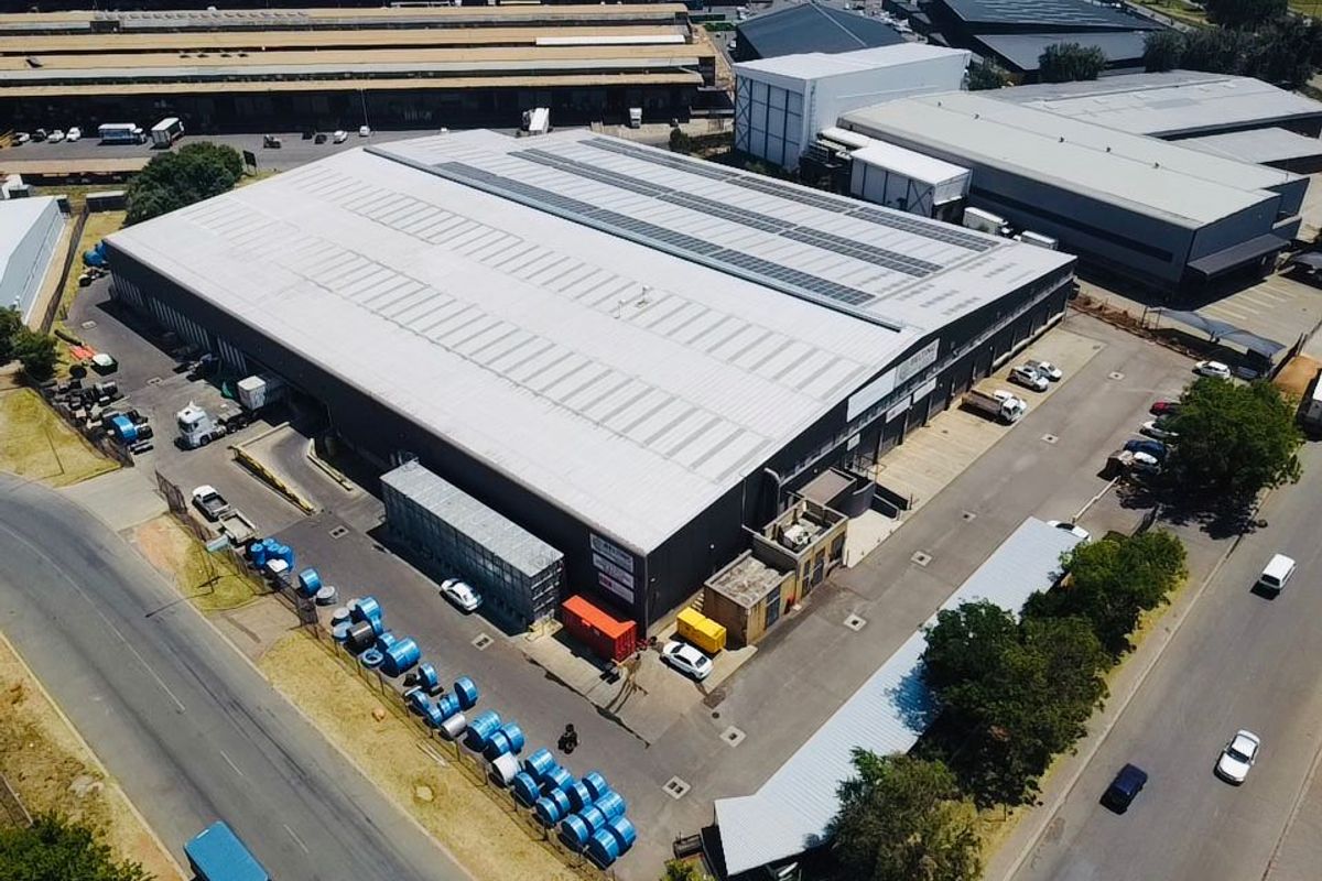 Aerial view of a large industrial warehouse facility featuring a metal roof, skylights, and dedicated loading and parking areas within a secure perimeter.