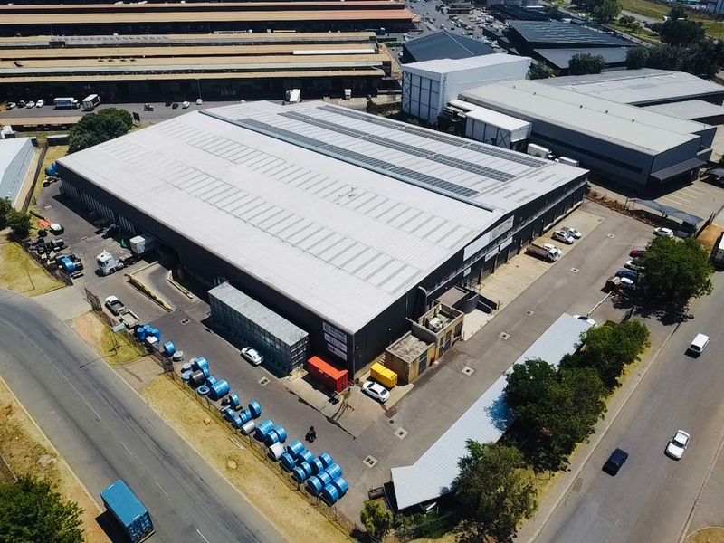 Aerial view of a large industrial warehouse facility featuring a metal roof, skylights, and dedicated loading and parking areas within a secure perimeter.
