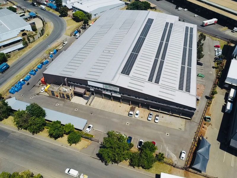 Aerial view of a large industrial warehouse facility featuring a metal roof with integrated solar panels, loading bays, and extensive paved parking.