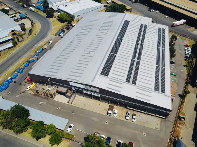 Aerial view of an industrial warehouse facility featuring a large metal roof with integrated solar panels and dedicated loading bay access.
