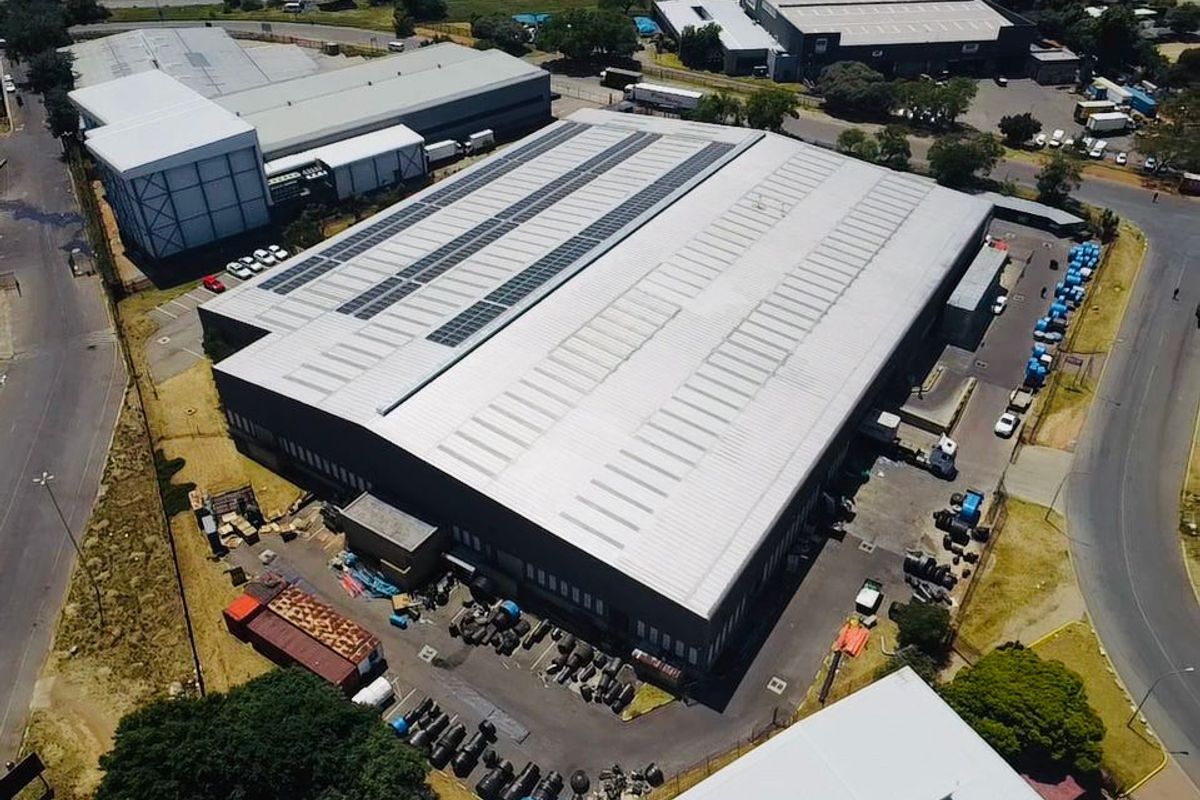 Aerial view of a large industrial warehouse facility featuring a metal roof with integrated solar panels and a paved yard area.