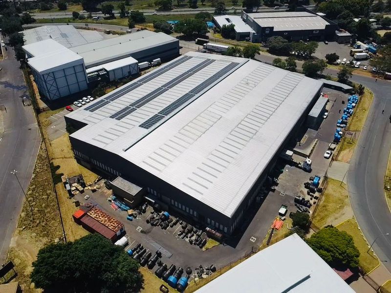 Aerial view of a large industrial warehouse facility featuring a metal roof with integrated solar panels and a paved yard area.