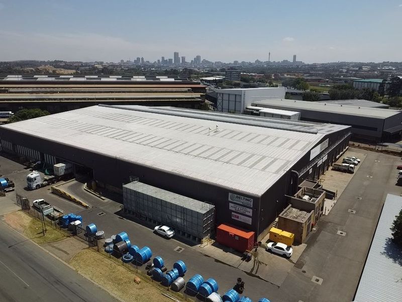 Aerial view of a large industrial warehouse facility featuring a metal roof, loading bays, and an expansive paved yard area.