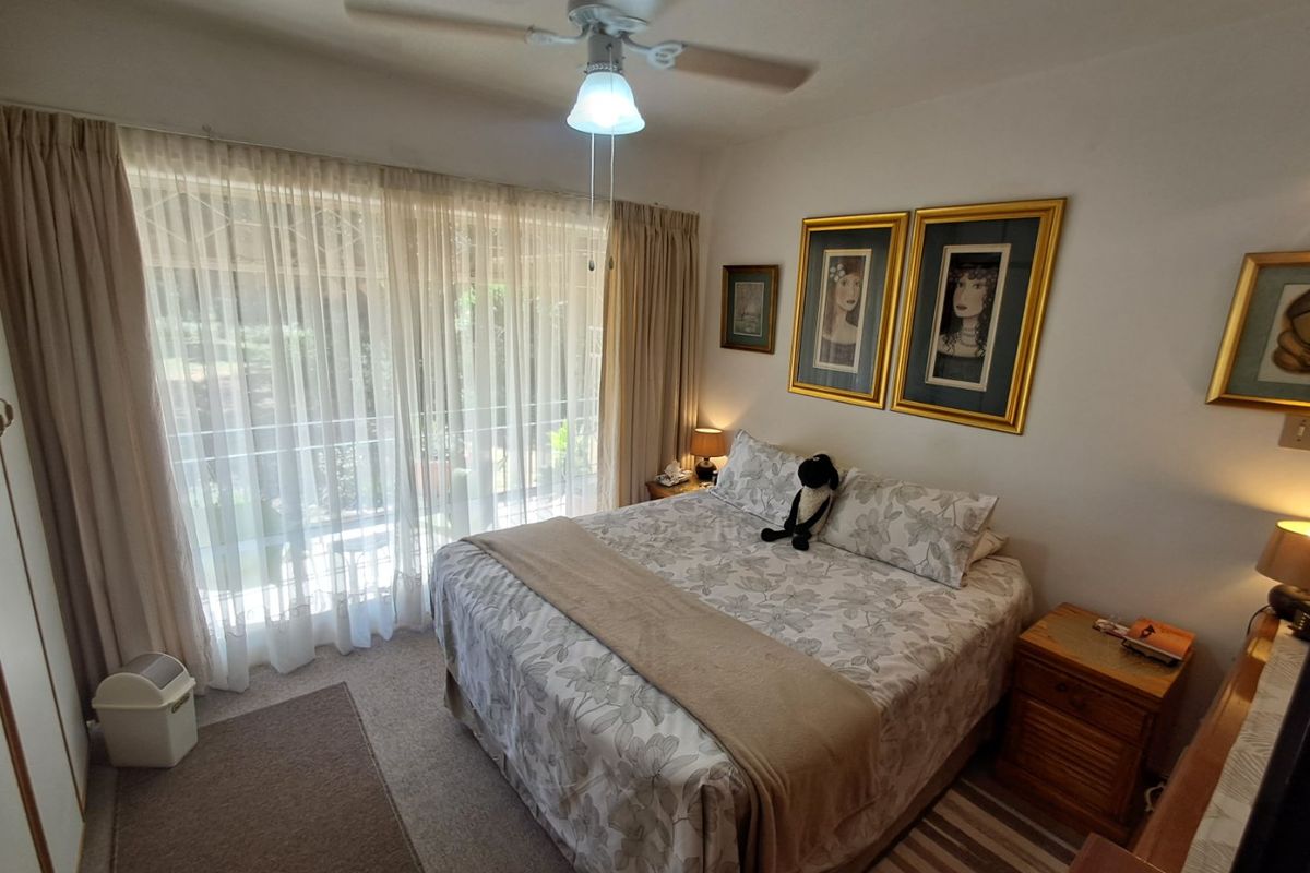 A comfortable bedroom featuring a ceiling fan, carpeted flooring, and a large sliding glass door that provides access to an outdoor balcony area.