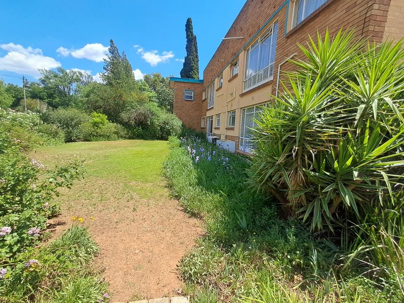 Rear view of the apartment building featuring a brick facade, large windows, and an established garden area with lawn.
