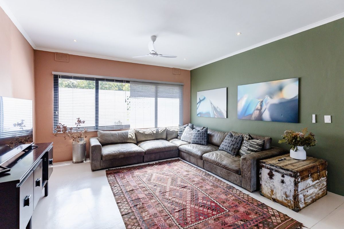 A well-maintained living room featuring a ceiling fan, recessed lighting, and dual-tone painted walls with large windows and venetian blinds.