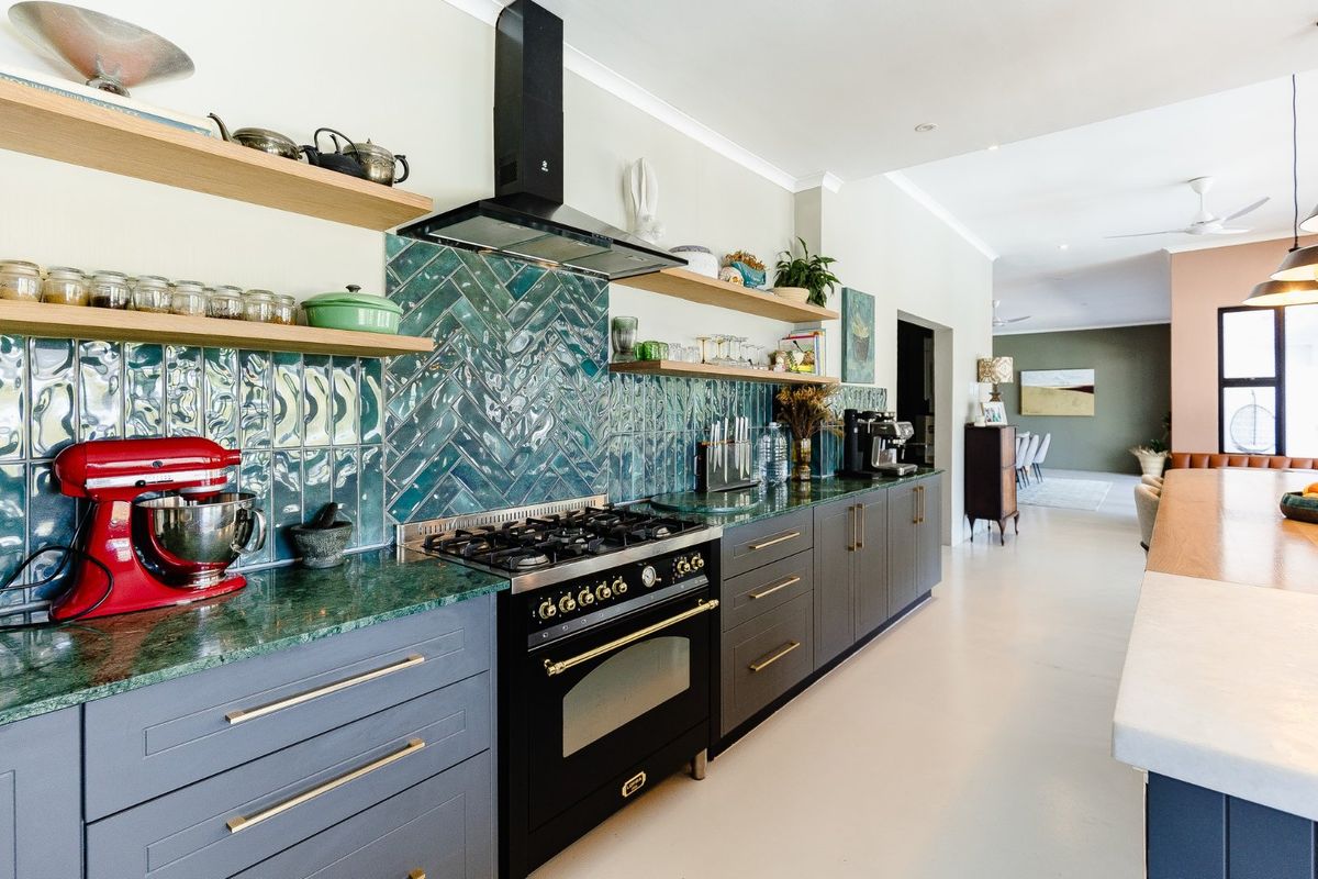 Modern kitchen featuring dark grey cabinetry, green stone countertops, a striking herringbone tile backsplash, and a professional-style gas range with extractor fan.