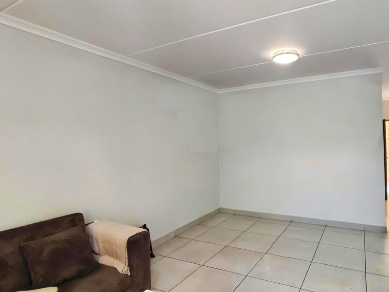 A neutrally painted living area featuring tiled flooring, ceiling cornicing, and a flush mount light fixture, offering a clean and functional space.