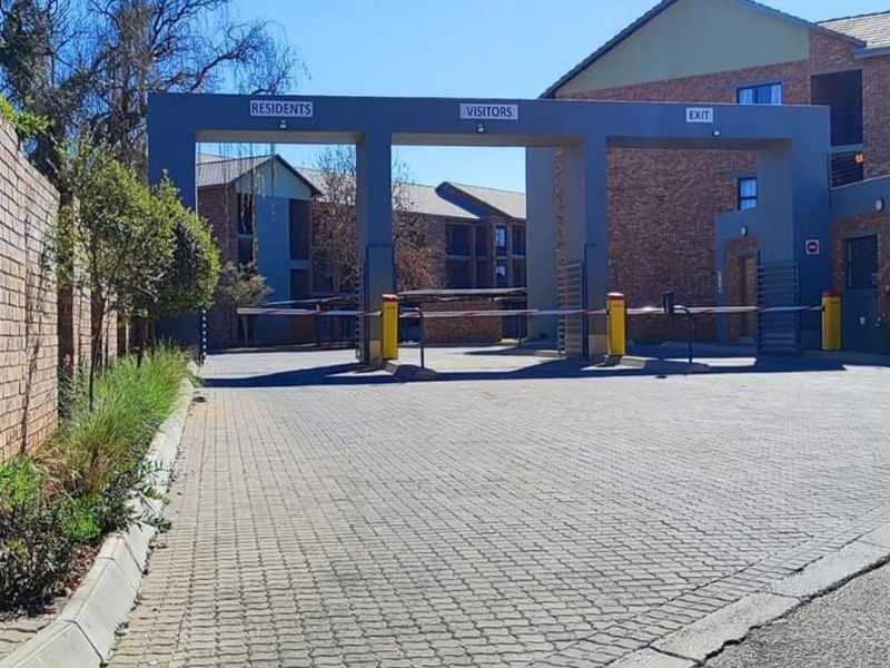The entrance to the apartment complex features a secure access-controlled boom gate system with designated lanes for residents and visitors.