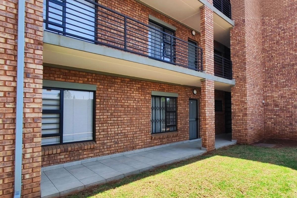 Exterior view of a multi-story apartment building featuring face brick construction, a ground-level tiled patio, and secure metal balcony railings.