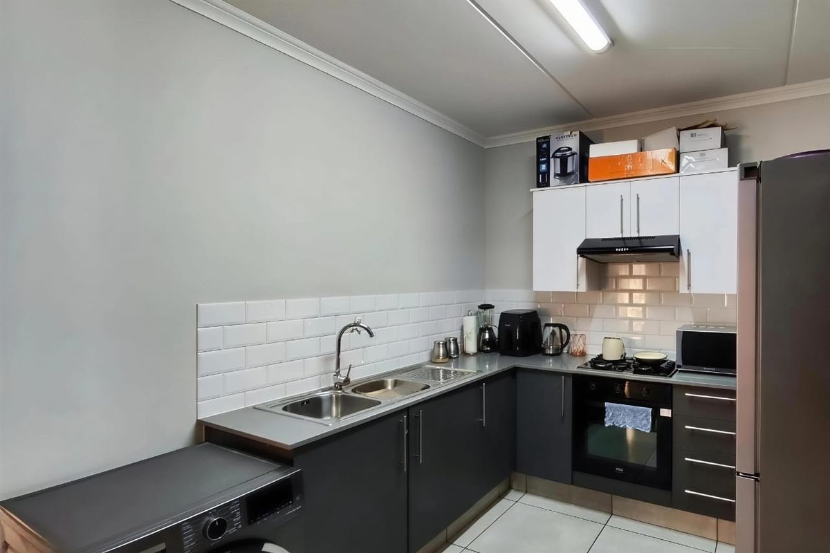 A functional kitchen featuring dark lower cabinetry, white upper cabinets, subway tile backsplash, stainless steel sink, and integrated oven with gas hob.