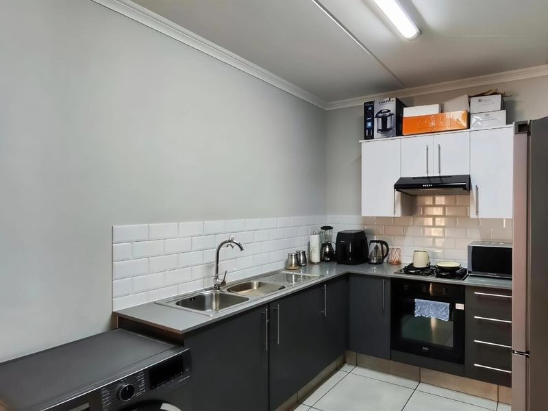 A functional kitchen featuring dark lower cabinetry, white upper cabinets, subway tile backsplash, stainless steel sink, and integrated oven with gas hob.