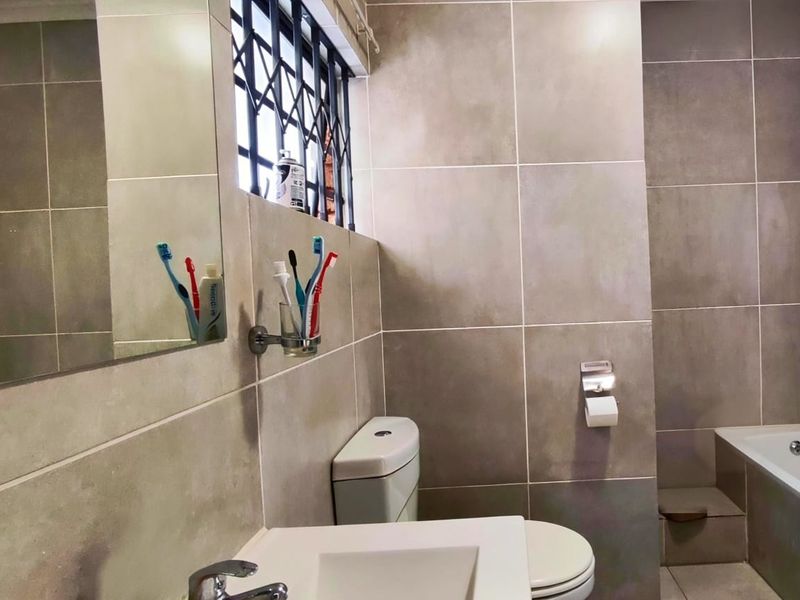 A modern bathroom featuring large format grey wall tiles, a built-in bathtub, a wall-mounted basin, and a toilet.